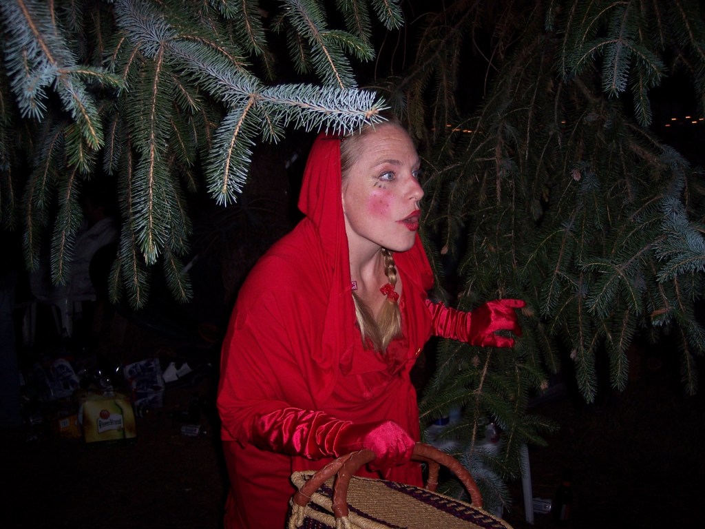 A woman dressed like Little Red Riding Hood holds a basket as she looks walks though the woods.