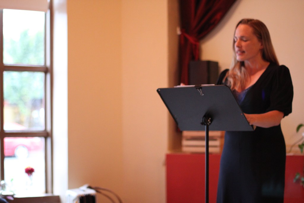 A woman in a black dress is standing behind a music stand. She is reciting a poem.