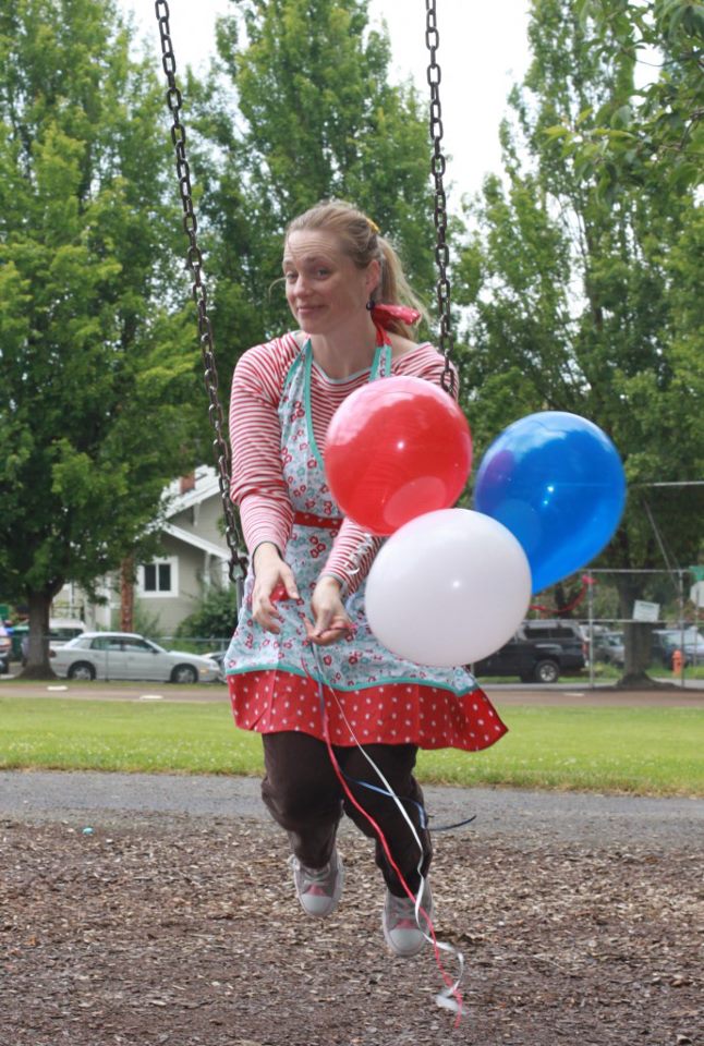 A young woman on a swing holding three balloons colored red, white and blue.