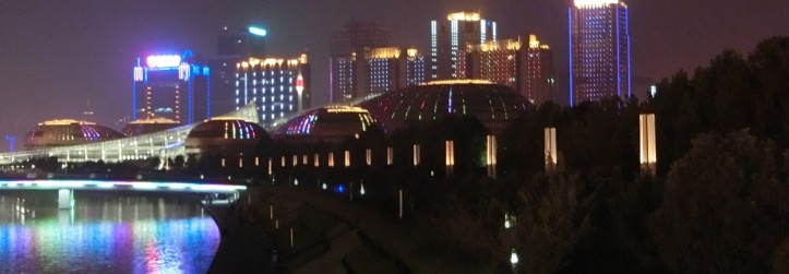 The Zhengzhou international conventaion center lit up at night with glowing purple, pink and blue colored lights.