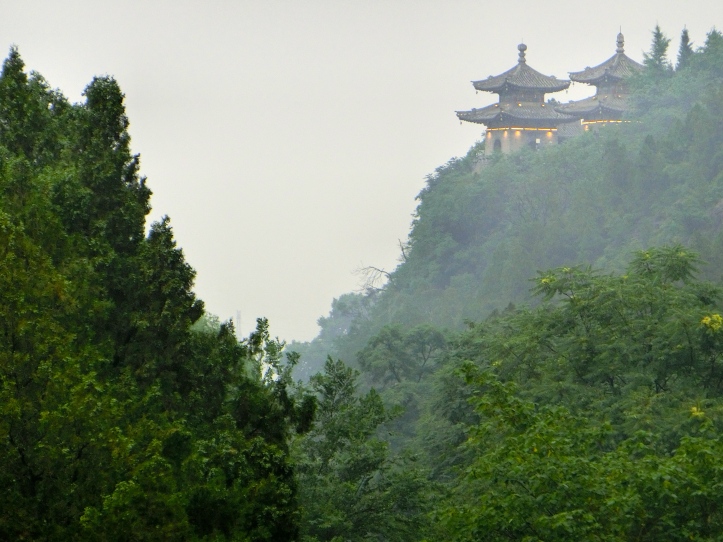 Two traditional Chinese buildings built on a lush green cliffside. 