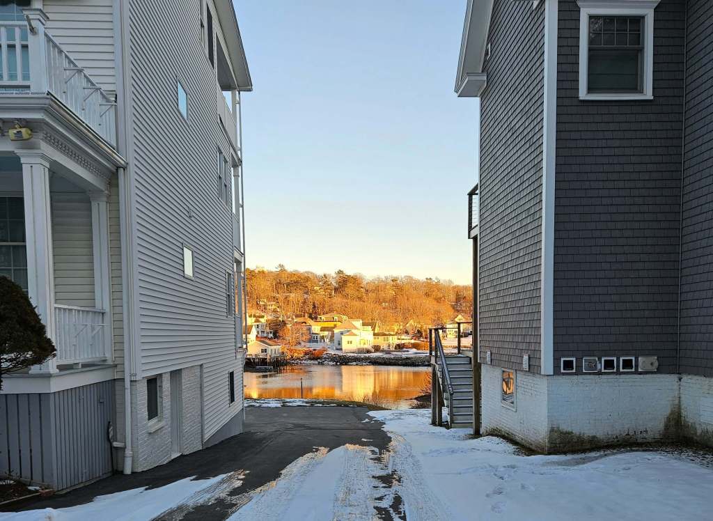 Two house frame and alleyway that offers a view of the sun soaked golden harbor and house in the distance.