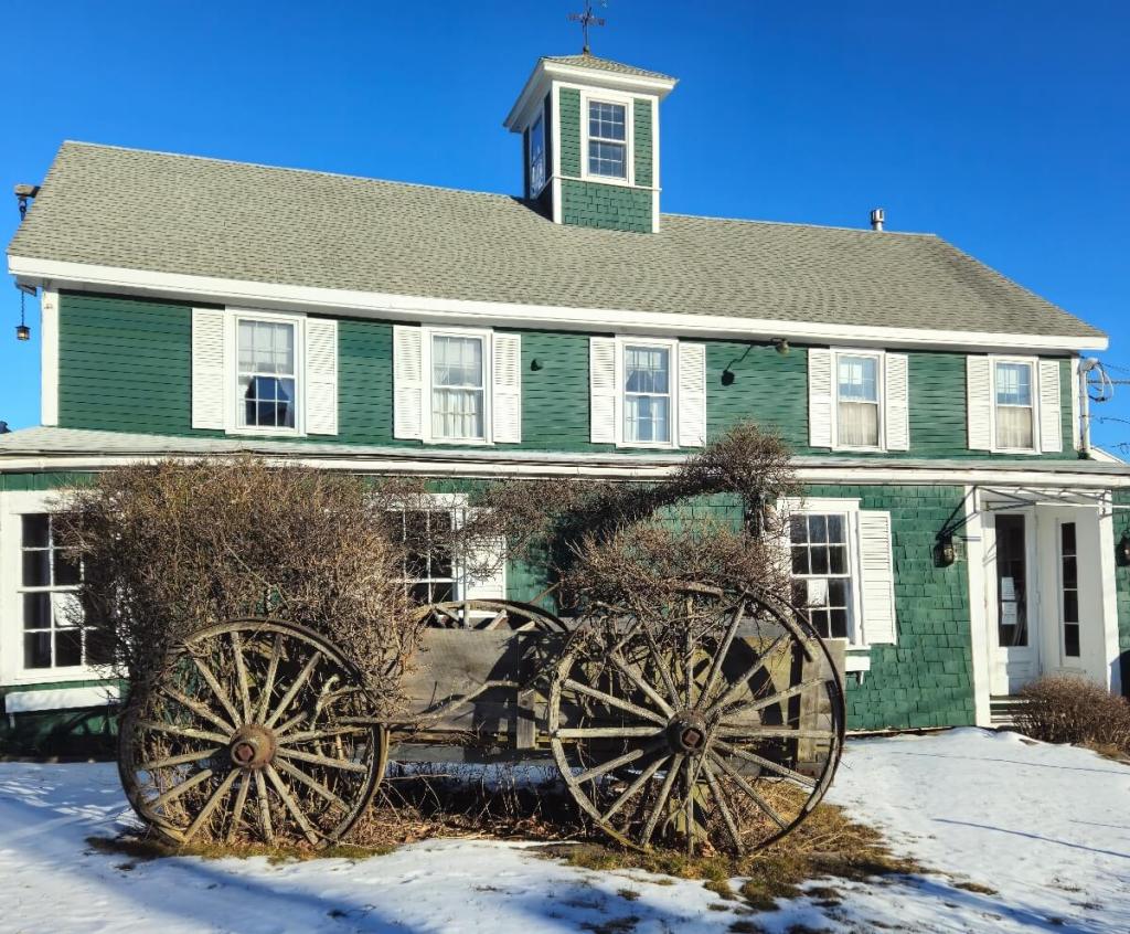 Green house with white trim. An old wagon sits on a snow covered lawn in front of the house.
