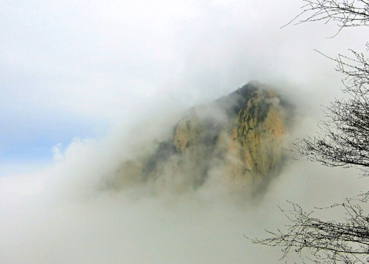 A peek of a mountain top through the clouds from 1,000 meters up.