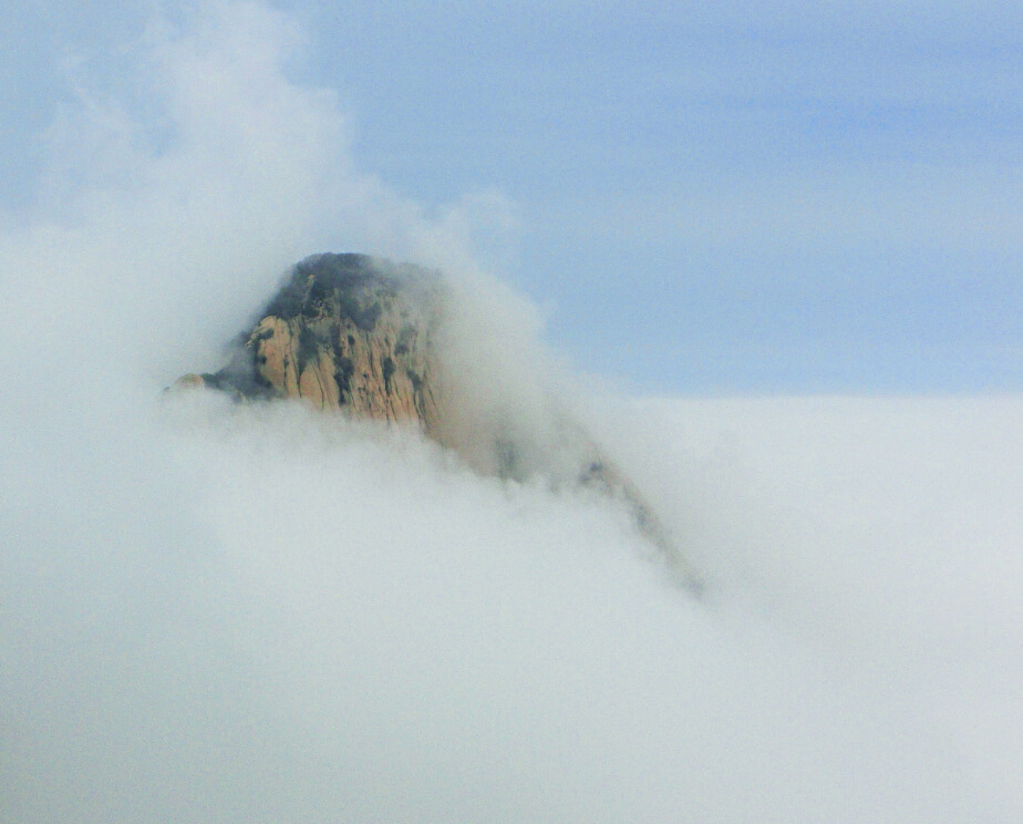 A close-up of a mountain peak in China surrounded by cloudes